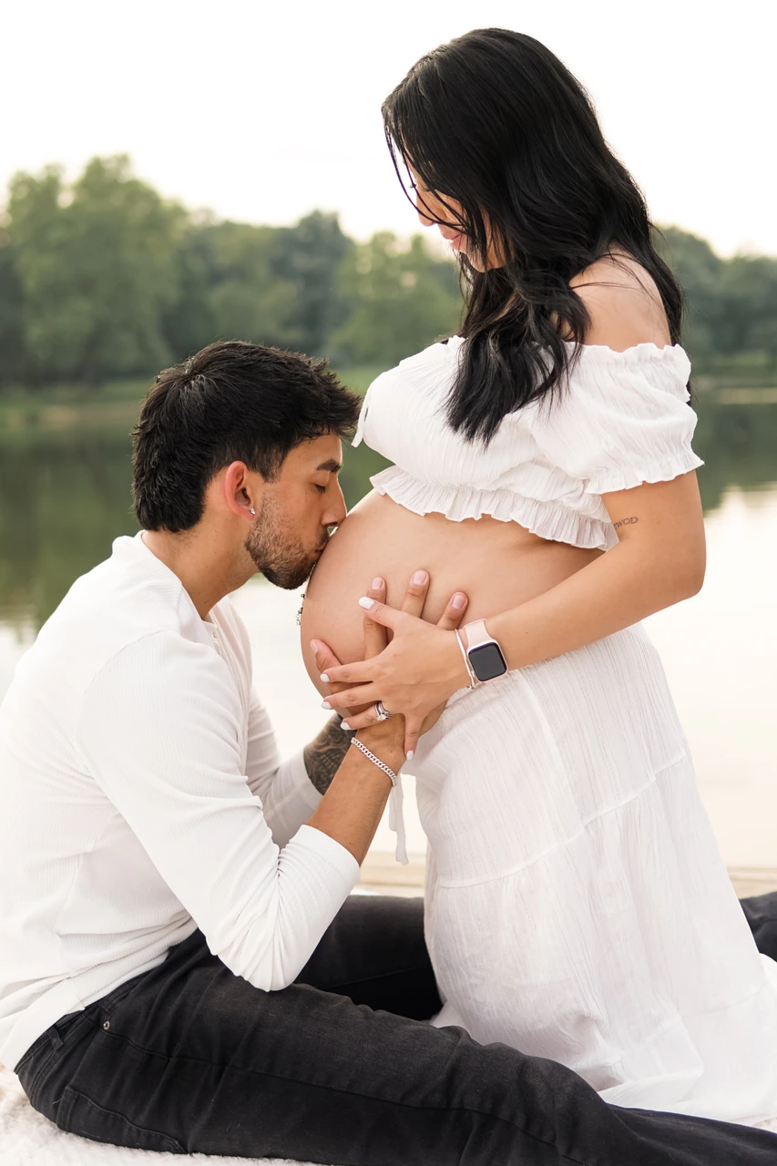 Man kissing his partner’s belly during their lakeside maternity session