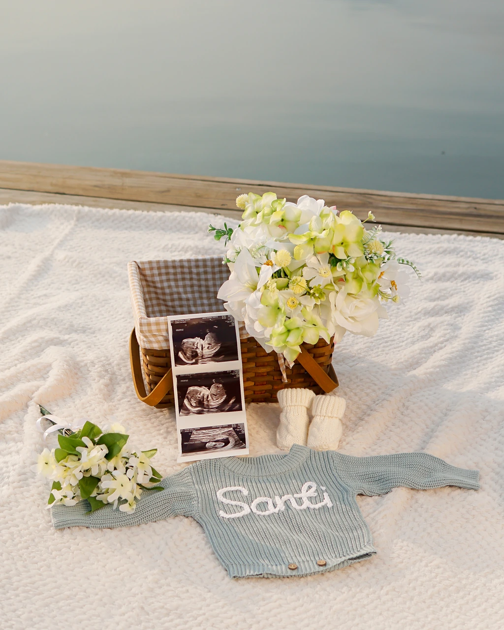 Ultrasound photos, flowers, baby booties and a blue Santi sweater arranged on a blanket