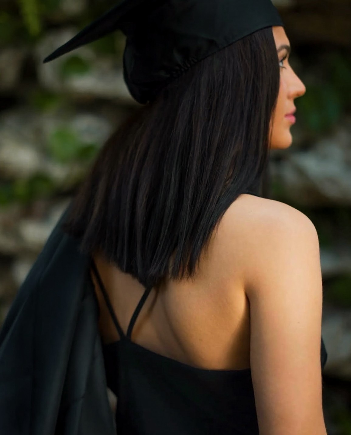 Profile portrait of a graduate in a black cap and dress looking over the shoulder