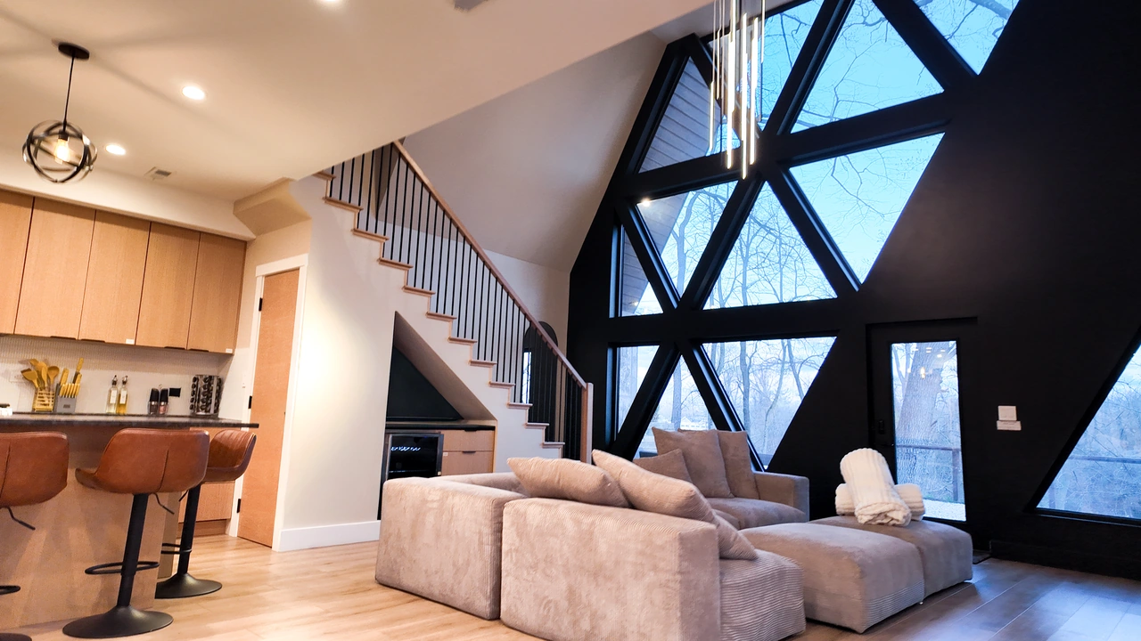 Double-height living room with geometric windows, a sectional sofa and an open staircase