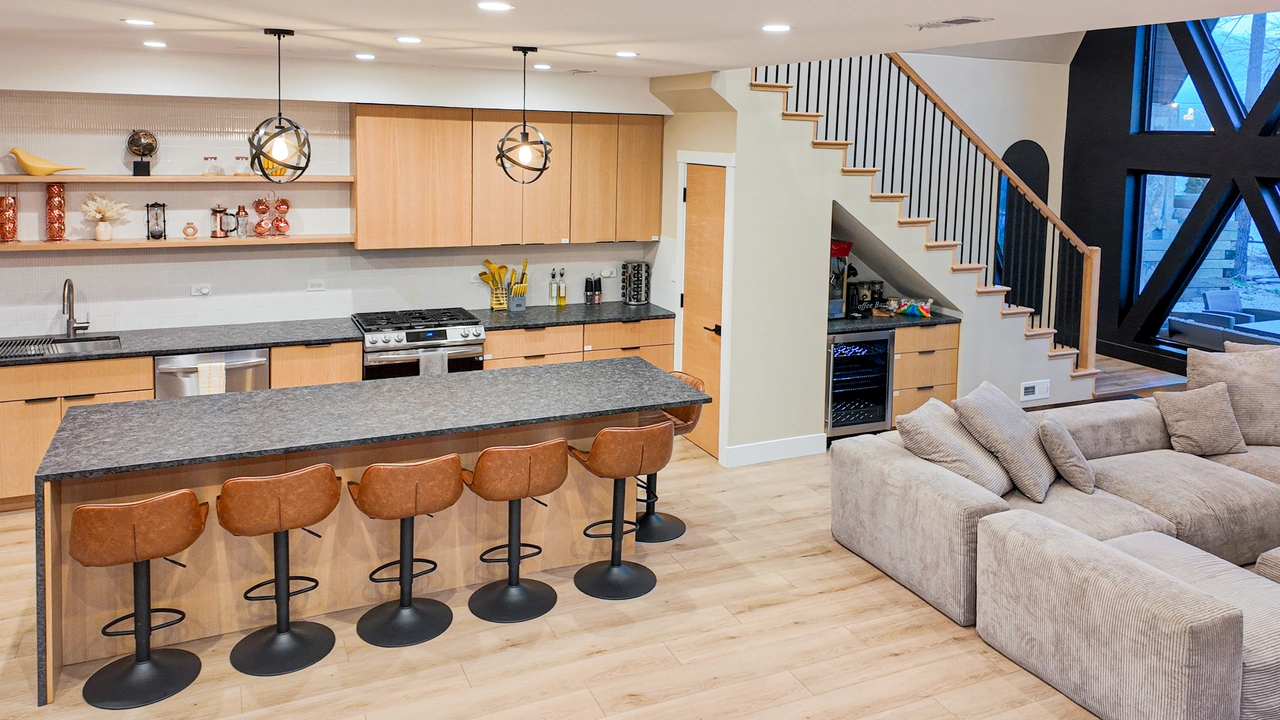 Open-plan kitchen and living area with a stone island, leather stools and wood cabinetry